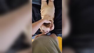 A red-haired girl in glasses and a short dress sucks a dick of a boyfriend standing in front of the bed