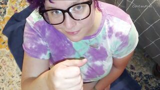 A bespectacled crumpet in a T-shirt and dyed curls sucks off her roommate's cock while sitting on the floor near the window
