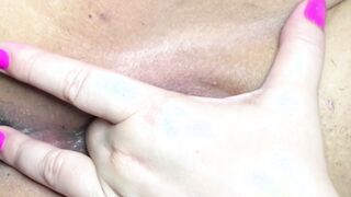 Dama morena con manicura rosa se masturba el coño afeitado con los dedos frente a la lente de la cámara