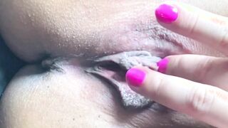 Dama morena con manicura rosa se masturba el coño afeitado con los dedos frente a la lente de la cámara
